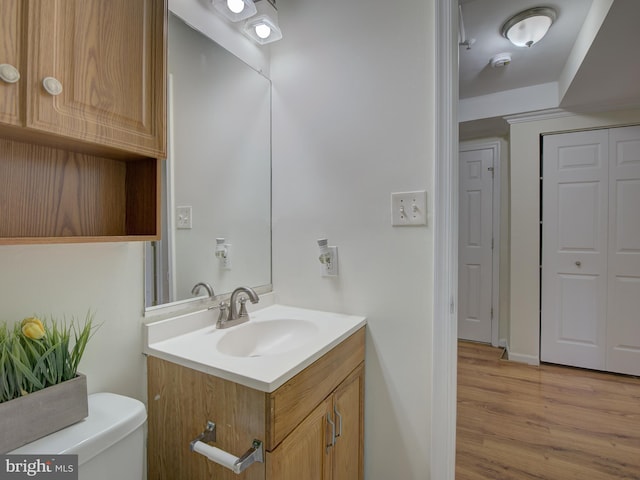 bathroom featuring toilet, a closet, wood finished floors, and vanity