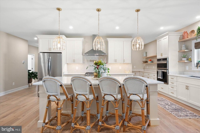 kitchen with light hardwood / wood-style flooring, hanging light fixtures, appliances with stainless steel finishes, and wall chimney exhaust hood