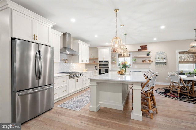 kitchen with wall chimney exhaust hood, appliances with stainless steel finishes, light hardwood / wood-style floors, a center island, and a breakfast bar