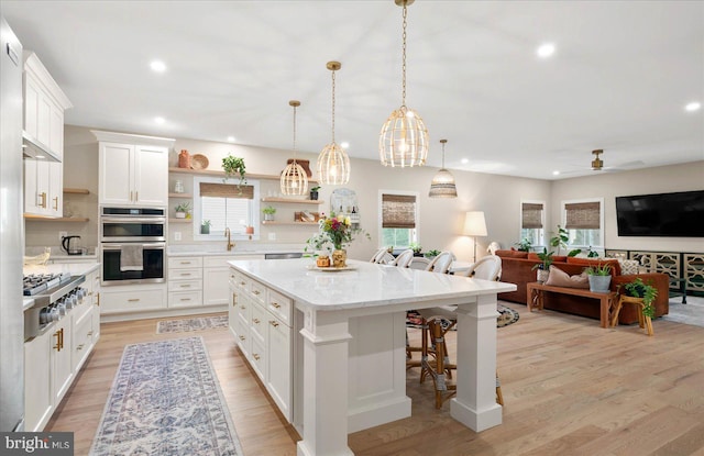 kitchen featuring light hardwood / wood-style flooring, a kitchen bar, a center island, ceiling fan, and appliances with stainless steel finishes