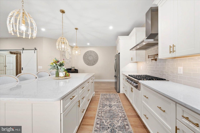 kitchen featuring a kitchen island, white cabinets, wall chimney range hood, appliances with stainless steel finishes, and light wood finished floors