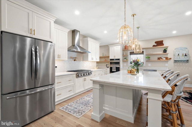 kitchen featuring white cabinetry, stainless steel appliances, wall chimney exhaust hood, a breakfast bar area, and light hardwood / wood-style floors