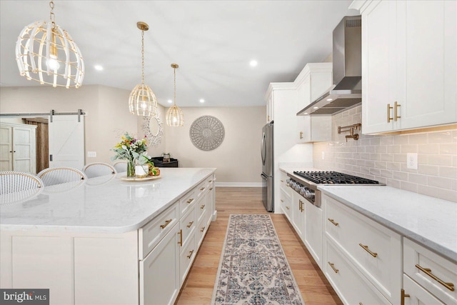 kitchen featuring light stone countertops, appliances with stainless steel finishes, a center island, a barn door, and wall chimney range hood