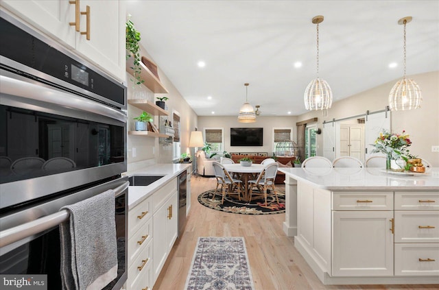 kitchen with light wood finished floors, a barn door, white cabinets, decorative light fixtures, and recessed lighting