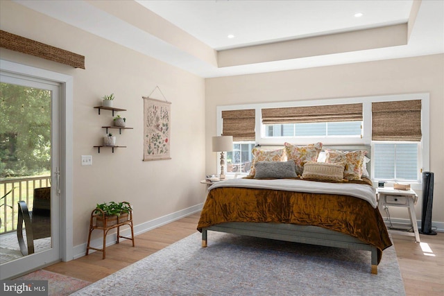 bedroom featuring light hardwood / wood-style flooring, a tray ceiling, multiple windows, and access to outside