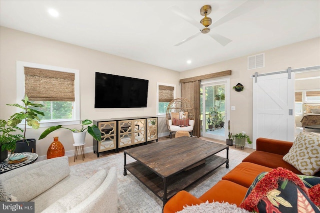 living room featuring a barn door, visible vents, ceiling fan, and baseboards