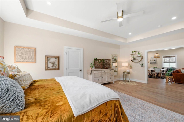 bedroom with light wood-type flooring, a tray ceiling, and ceiling fan