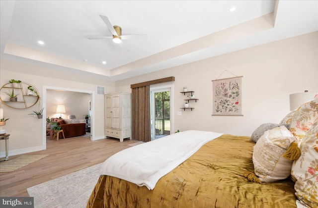 bedroom featuring light hardwood / wood-style flooring, ceiling fan, a raised ceiling, and access to outside