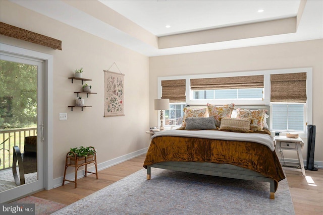 bedroom with access to outside, baseboards, light wood-style flooring, and a tray ceiling