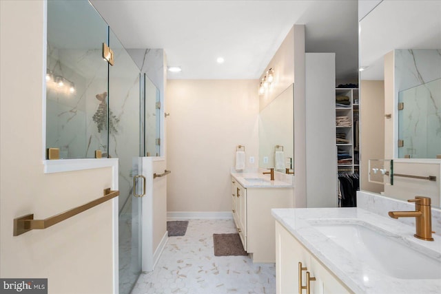 full bathroom with a walk in closet, two vanities, a sink, and a marble finish shower