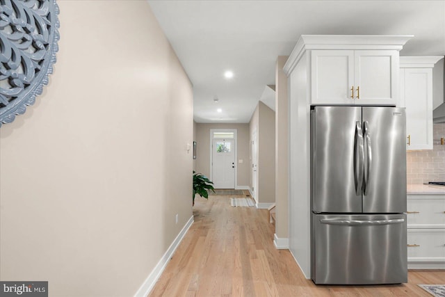 kitchen featuring light hardwood / wood-style flooring, stainless steel refrigerator, backsplash, and white cabinets