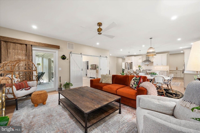 living room with a barn door, ceiling fan, and light wood-type flooring