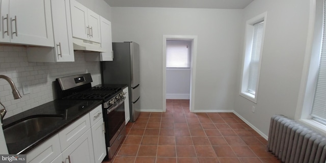 kitchen featuring dark tile patterned flooring, radiator heating unit, stainless steel appliances, under cabinet range hood, and white cabinetry