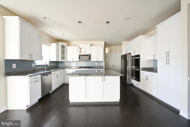 kitchen featuring decorative backsplash, dark hardwood / wood-style floors, pendant lighting, appliances with stainless steel finishes, and a center island