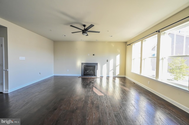 unfurnished living room featuring dark wood-style floors, ceiling fan, a glass covered fireplace, and baseboards