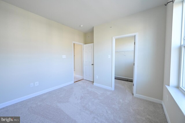 unfurnished bedroom featuring a spacious closet, a closet, and light carpet