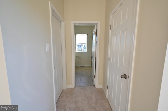 corridor featuring light carpet, light tile patterned floors, and baseboards