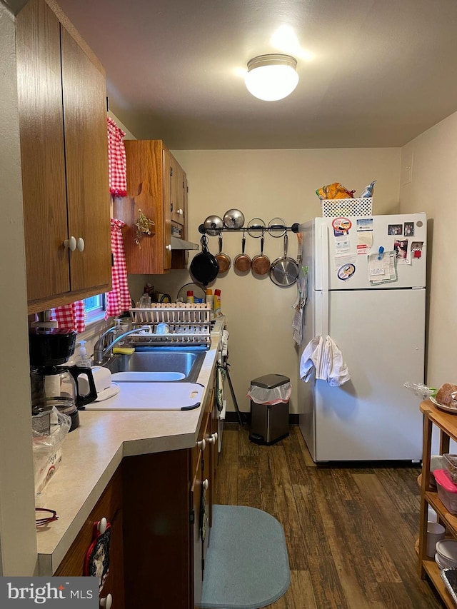 kitchen with under cabinet range hood, dark wood-style flooring, light countertops, freestanding refrigerator, and brown cabinets