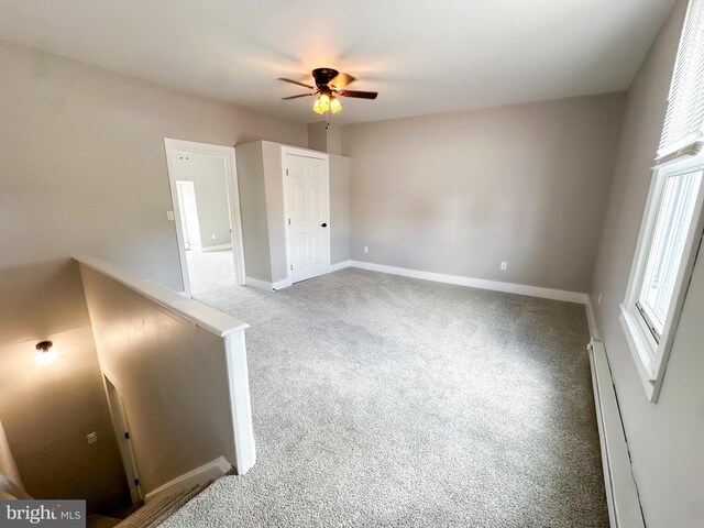 unfurnished bedroom with ceiling fan, a baseboard heating unit, light colored carpet, and multiple windows