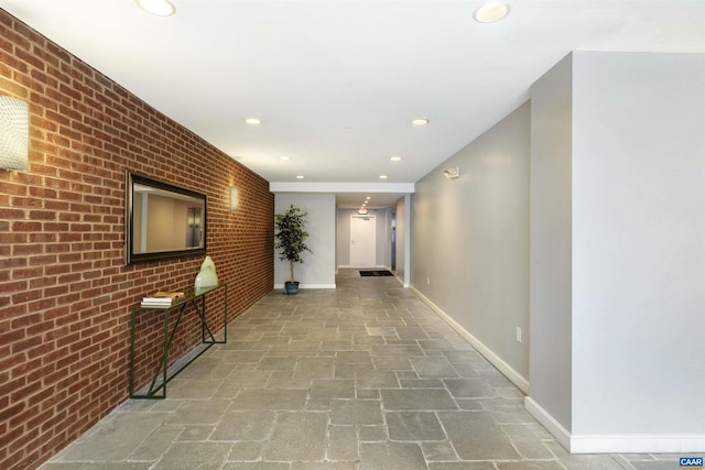 hall featuring recessed lighting, stone floors, baseboards, and brick wall