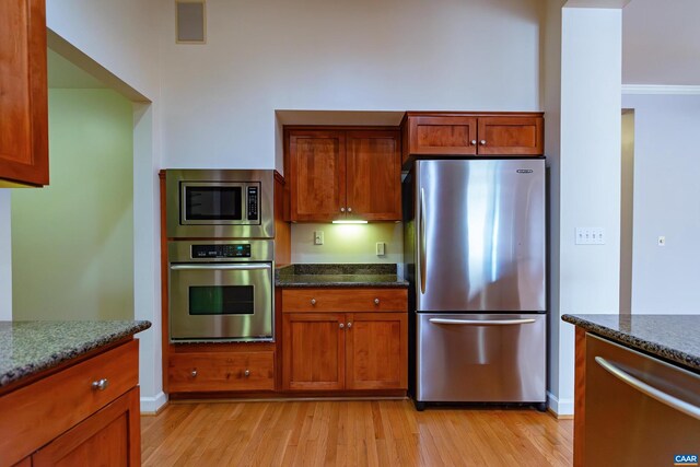 kitchen featuring dark stone counters, kitchen peninsula, light hardwood / wood-style flooring, and stainless steel oven