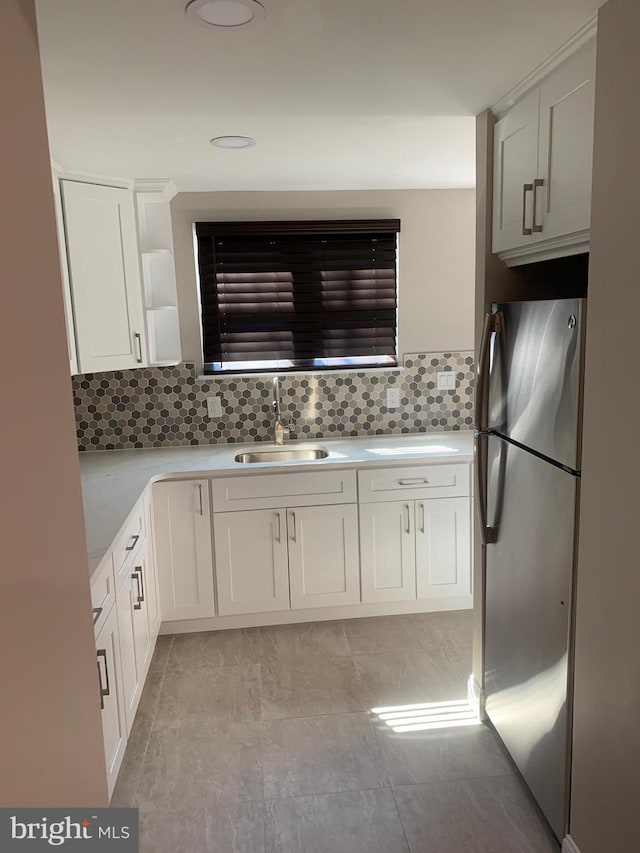 kitchen with freestanding refrigerator, white cabinets, light countertops, and a sink