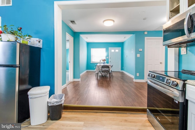 kitchen with appliances with stainless steel finishes, light hardwood / wood-style flooring, and white cabinets