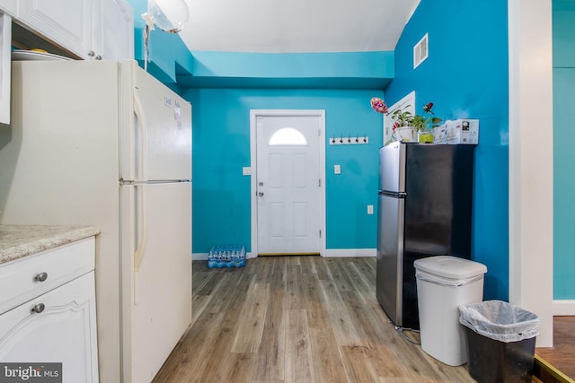 kitchen with stainless steel fridge, light wood-type flooring, white refrigerator, and white cabinets