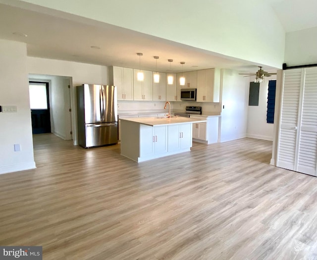 kitchen featuring white cabinets, hanging light fixtures, light hardwood / wood-style flooring, stainless steel appliances, and an island with sink