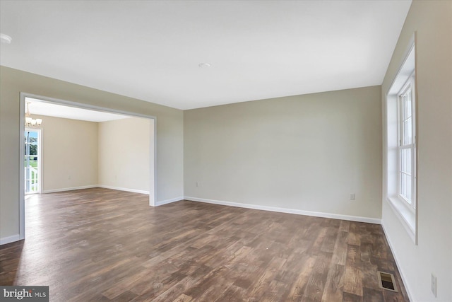 spare room with a notable chandelier, dark wood-type flooring, visible vents, and baseboards