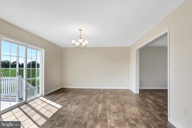 spare room with a chandelier, dark wood finished floors, and baseboards