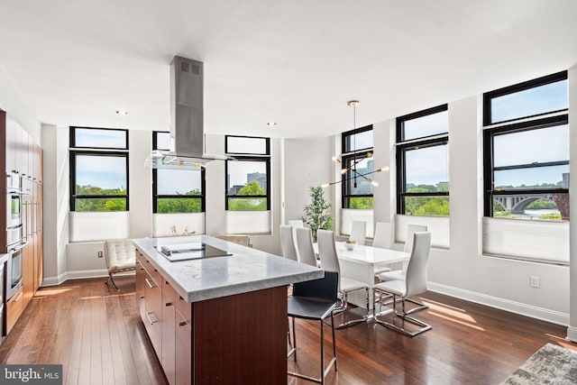 kitchen with island range hood, an island with sink, light stone countertops, dark wood-type flooring, and black electric cooktop