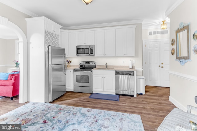 kitchen with sink, white cabinetry, stainless steel appliances, hardwood / wood-style floors, and ornamental molding