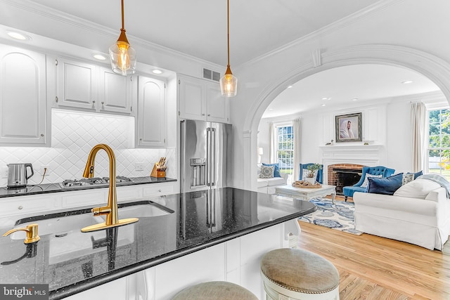 kitchen featuring dark stone counters, light wood-type flooring, white cabinets, high quality fridge, and a brick fireplace