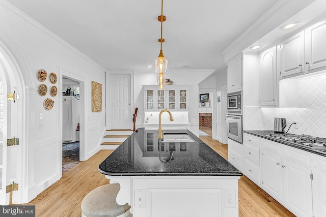 kitchen with appliances with stainless steel finishes, a kitchen island with sink, dark stone counters, and light hardwood / wood-style flooring