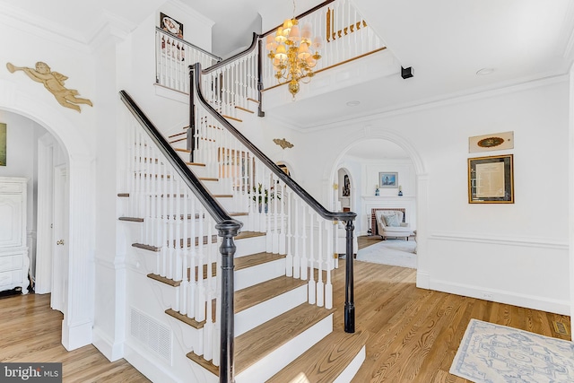 staircase featuring ornamental molding, an inviting chandelier, a towering ceiling, and hardwood / wood-style flooring