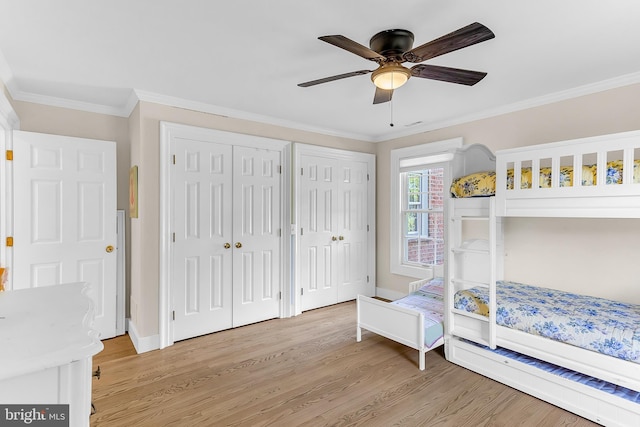 bedroom featuring light wood-type flooring, two closets, ceiling fan, and crown molding