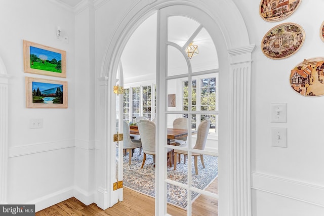 interior space with an inviting chandelier, ornate columns, hardwood / wood-style flooring, and crown molding