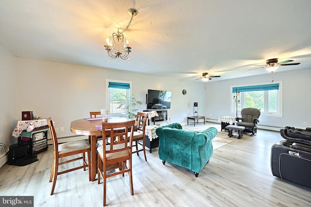 dining space featuring light wood-type flooring, a wealth of natural light, a baseboard heating unit, and ceiling fan with notable chandelier