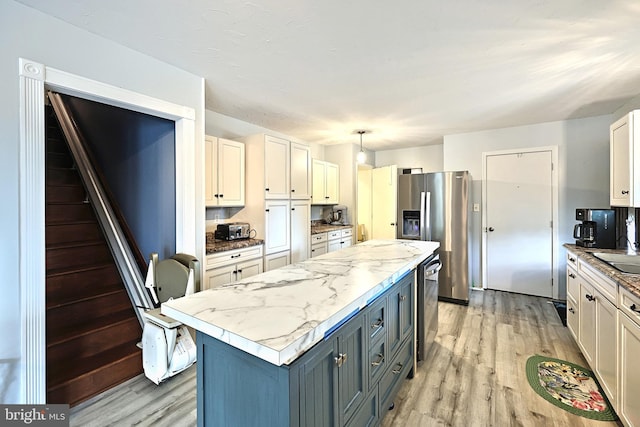 kitchen with light wood-type flooring, hanging light fixtures, light stone countertops, sink, and stainless steel fridge with ice dispenser