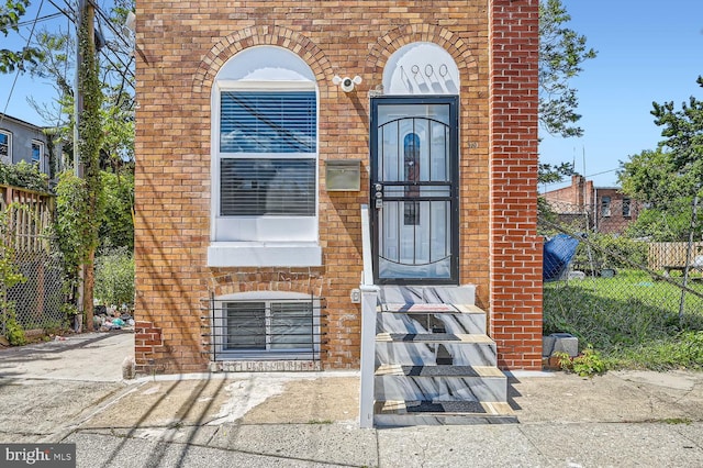 entrance to property featuring fence and brick siding