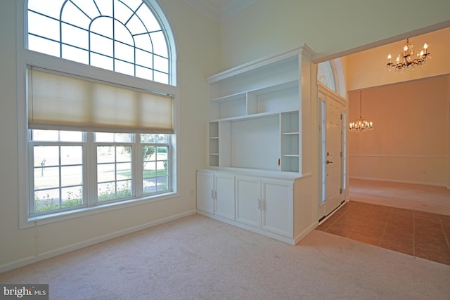 carpeted empty room featuring a notable chandelier, a towering ceiling, ornamental molding, tile patterned flooring, and baseboards