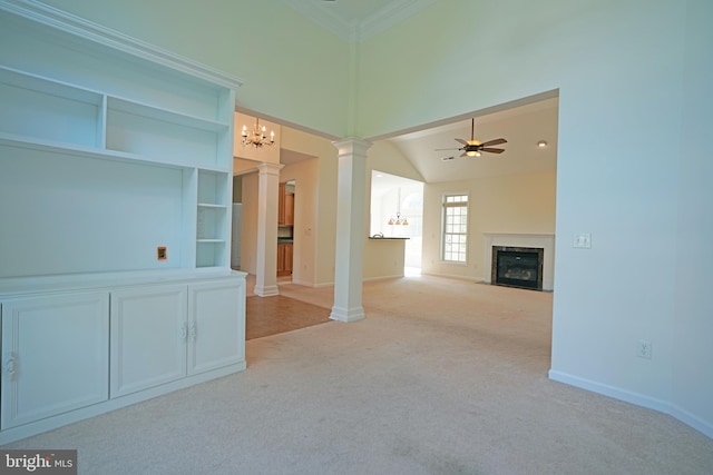 unfurnished living room featuring ceiling fan with notable chandelier, a fireplace, carpet flooring, a towering ceiling, and decorative columns