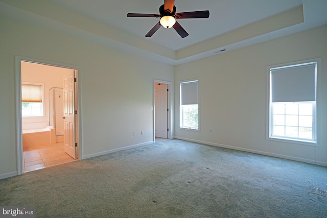 carpeted spare room featuring a wealth of natural light, ceiling fan, and a tray ceiling