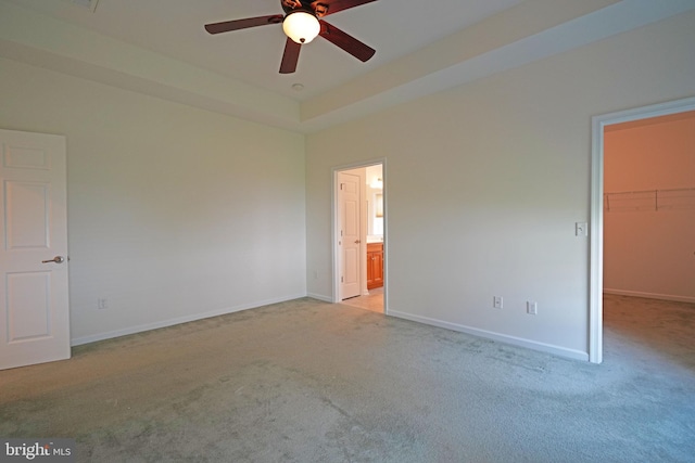 unfurnished bedroom featuring baseboards, a raised ceiling, a walk in closet, and light colored carpet