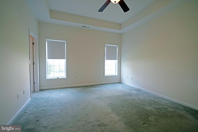 empty room with ceiling fan, light carpet, and a tray ceiling