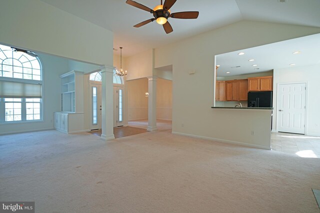 unfurnished living room with ceiling fan with notable chandelier, light colored carpet, high vaulted ceiling, and ornate columns