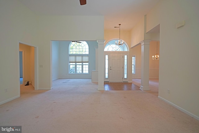 carpeted entrance foyer with a high ceiling, ceiling fan with notable chandelier, and decorative columns