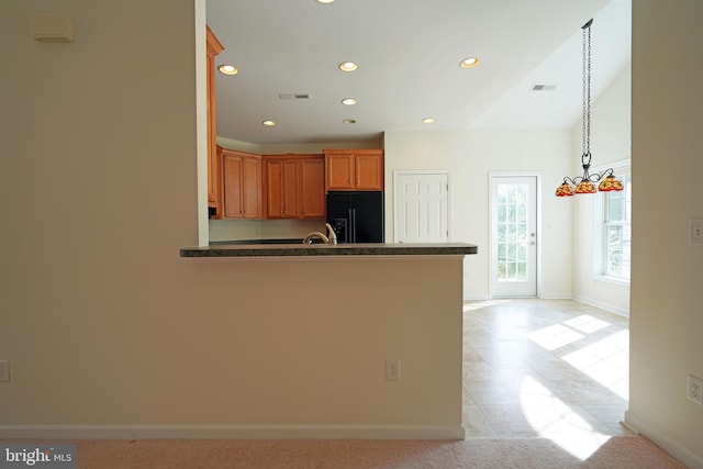 kitchen featuring pendant lighting, kitchen peninsula, light tile patterned floors, and black fridge