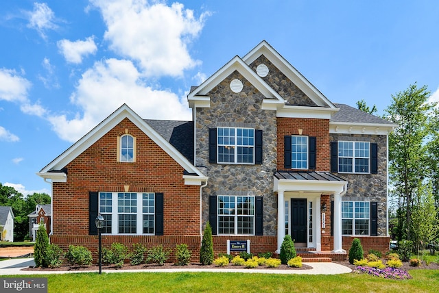 view of front facade featuring stone siding, metal roof, a standing seam roof, a front yard, and brick siding